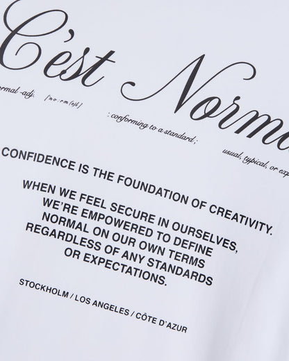 A close-up shot of the white fabric on The Première T-Shirt, highlighting the high-density matte print featuring the c'est normal artwork and accompanying text.