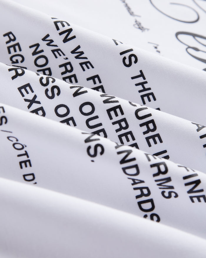 A close-up shot of the white heavyweight jersey fabric on The Première T-Shirt, highlighting the signature c'est normal artwork in a high-density matte black text print.