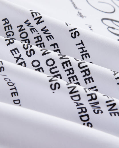 A close-up shot of the white heavyweight jersey fabric on The Première T-Shirt, highlighting the signature c'est normal artwork in a high-density matte black text print.