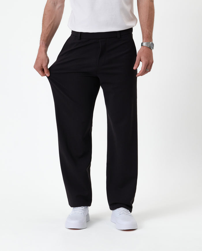 The Proper Pant Relaxed Straight Fit in black — pulling the fabric to show the stretch