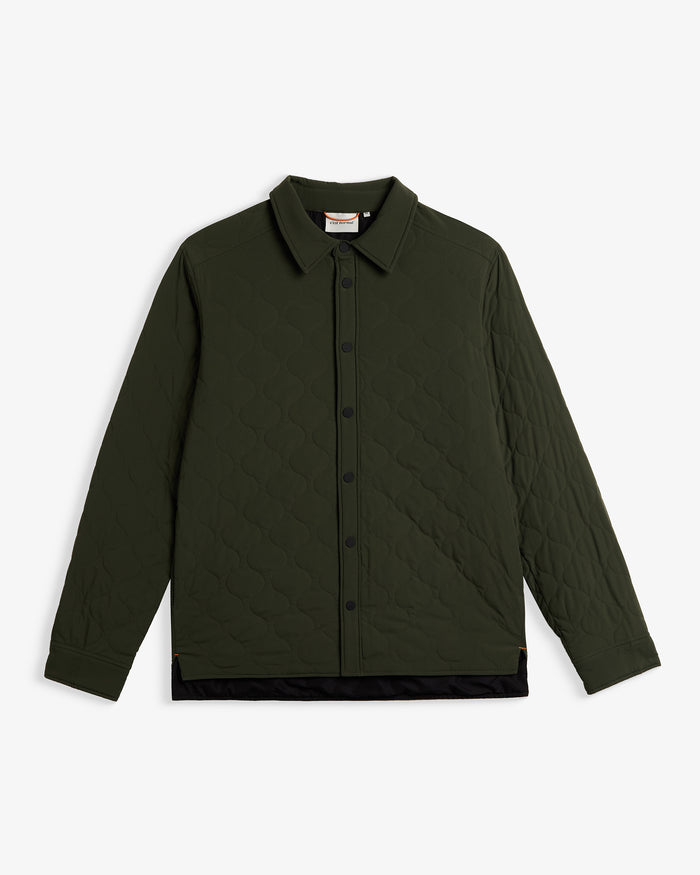 A front view of The Quilted Overshirt in Khaki, laid flat on a white background. The image highlights the signature wave quilting, the black button closure, and the c'est normal label at the inside of the neck.
