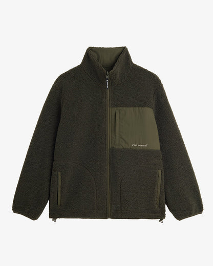 A front view of The Reversible Pile Jacket in Forest Green, laid flat on a white background. The image highlights the cozy pile fleece side, the zippered chest pocket with the c'est normal logo, and the zip hand pockets.