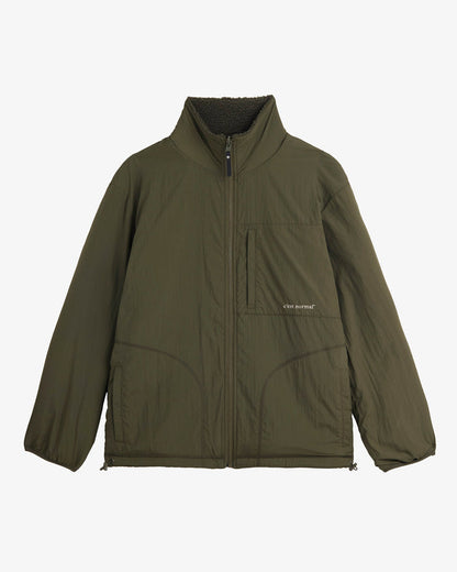A front view of The Reversible Pile Jacket in Forest Green, laid flat on a white background. The image showcases the smooth tech side, featuring a full front zipper, a zippered chest pocket with the c'est normal logo, and two hand pockets.