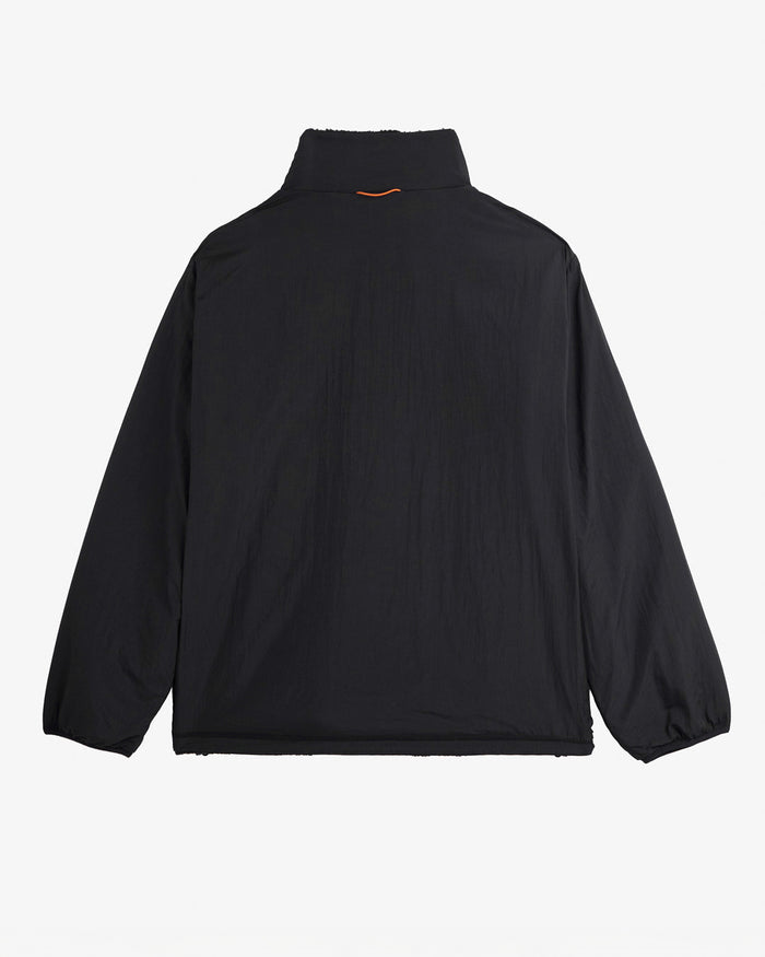 A back view of The Reversible Pile Jacket in black, laid flat on a white background. The image highlights the smooth tech side and an orange detail on the back of the collar.