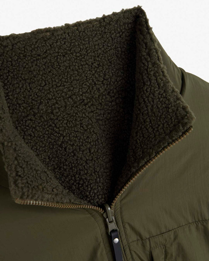 A detailed close-up of the collar of The Reversible Pile Jacket in forest green, laid flat on a white background. The image highlights the contrast between the smooth tech fabric exterior and the textured pile fleece lining, along with the partially open front zipper.
