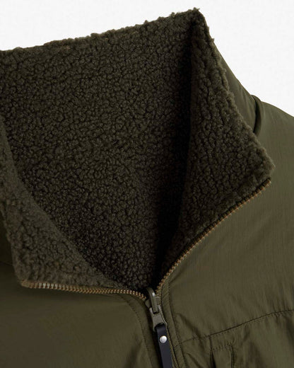 A detailed close-up of the collar of The Reversible Pile Jacket in forest green, laid flat on a white background. The image highlights the contrast between the smooth tech fabric exterior and the textured pile fleece lining, along with the partially open front zipper.