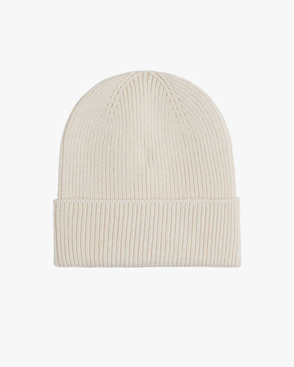 The Ribbed Beanie in cream, laid flat on a white background, highlighting its classic ribbed knit texture and folded brim. The tone on tone rubber tag with the c'est normal logo is not visible from this angle.
