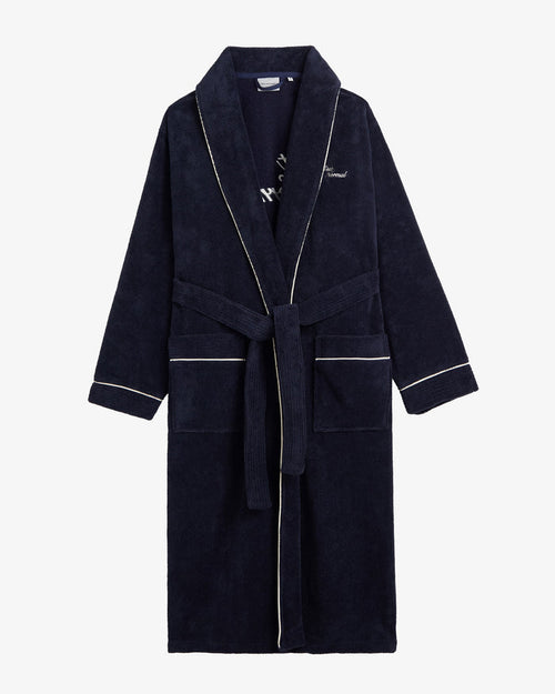 A front view of The Robe in navy, laid flat on a white background. The image highlights the tied belt, two front pockets, white piping, and the embroidered c'est normal logo on the chest.