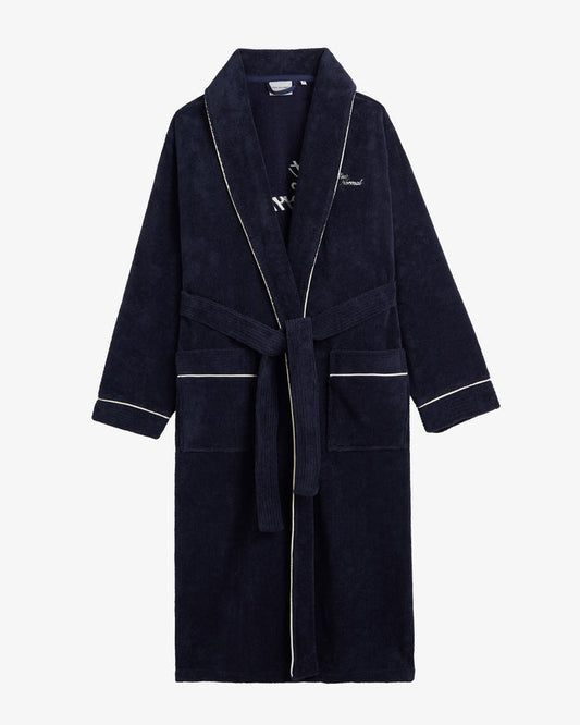 A front view of The Robe in navy, laid flat on a white background. The image highlights the tied belt, two front pockets, white piping, and the embroidered c'est normal logo on the chest.