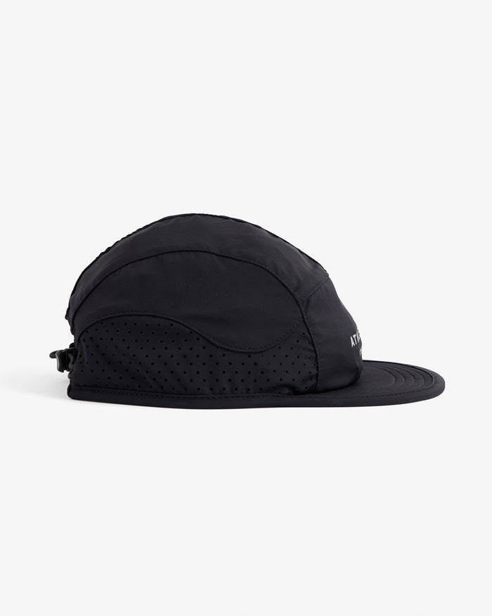 A side view of The Running Cap in black, laid flat on a white background. The image highlights the lightweight mesh side panels and the adjustable toggle closure at the back.