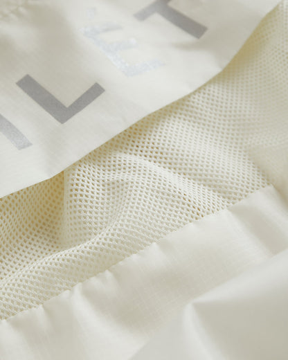 A detailed close-up of The Running Jacket in cream, highlighting the breathable mesh back ventilation panel and reflective silver lettering.