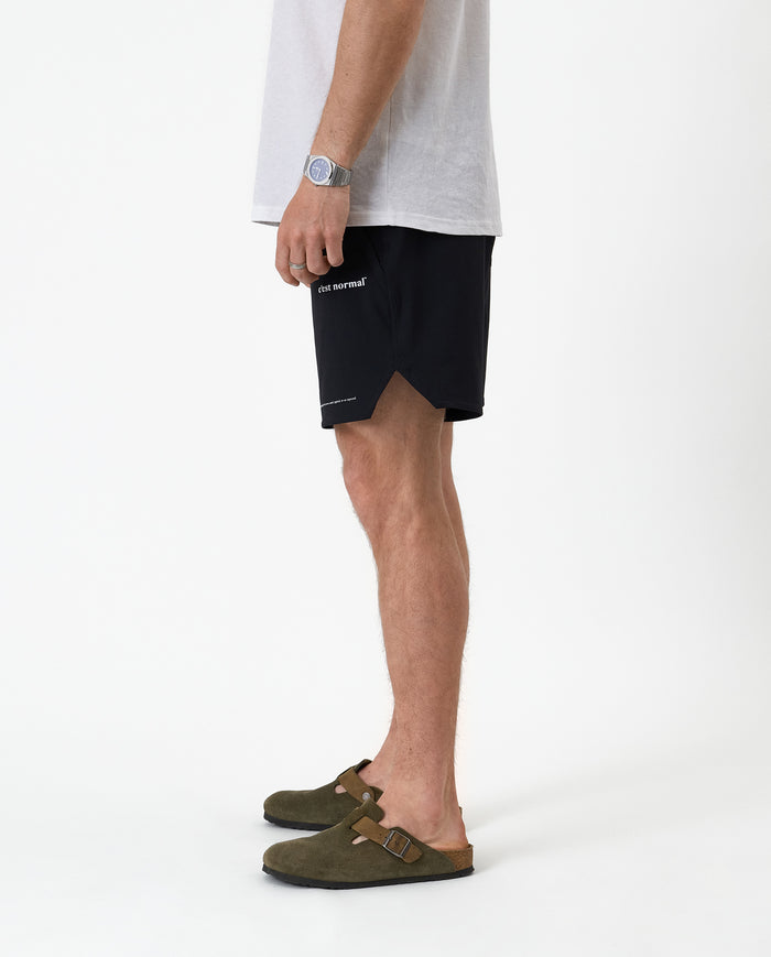 The Shorts in black — side view showing the notched hem and white C'est normal logo