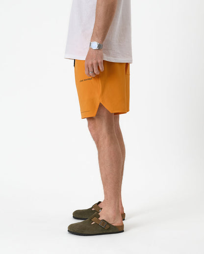 The Shorts in orange peel — side view showing the notched hem and black brand logo