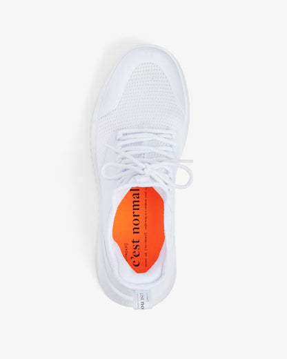A top-down view of The Sneakers 2.0 in white, laid flat on a white background. The image highlights the soft mesh upper, laces, and the bright orange insock featuring the c'est normal logo.