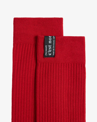 A detailed close-up of The Sock in red, focusing on the ribbed cuff and the black tag featuring the white c'est normal logo.