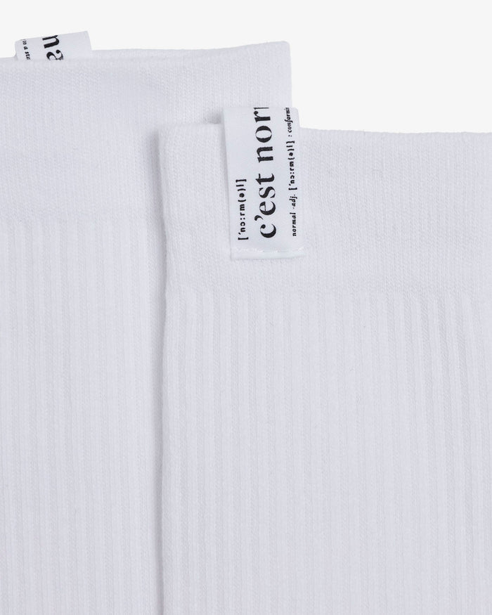 A detailed close-up of The Sock in white, focusing on the ribbed fabric and the cuff tag with the c'est normal logo.