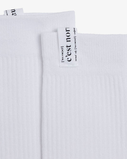 A detailed close-up of The Sock in white, focusing on the ribbed fabric and the cuff tag with the c'est normal logo.