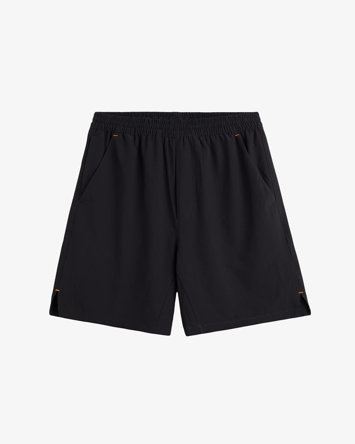 A front view of The Training Shorts in black, laid flat on a white background. The image highlights the elastic waistband, slanted side pockets, and side slits.