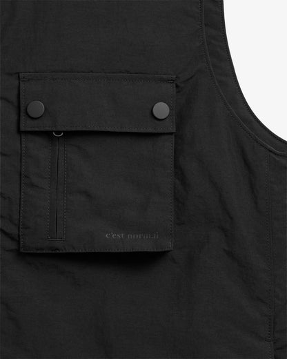 The Utility Vest in black — close-up of chest pocket with snap buttons and C'est normal branding