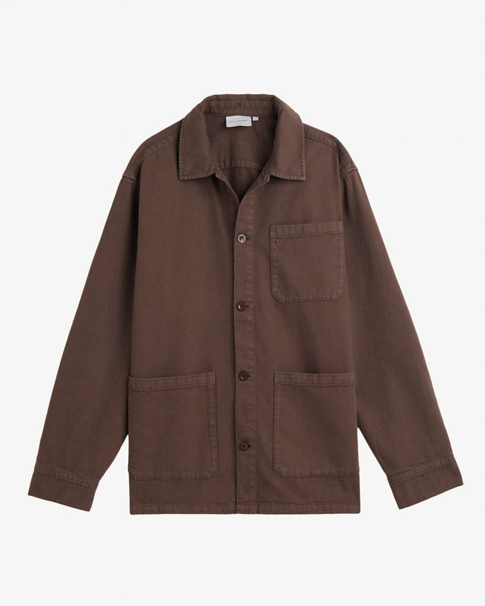 A front view of The Workwear Overshirt in brown, laid flat on a white background. The image highlights the button-up front, collar, and three patch pockets.
