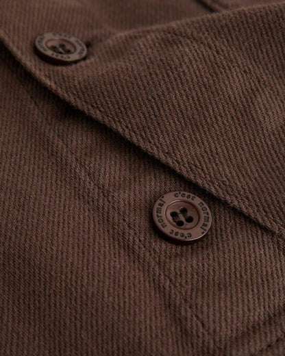 A close-up shot of The Workwear Overshirt in brown, focusing on the textured cotton fabric and the brown buttons engraved with the c'est normal logo.